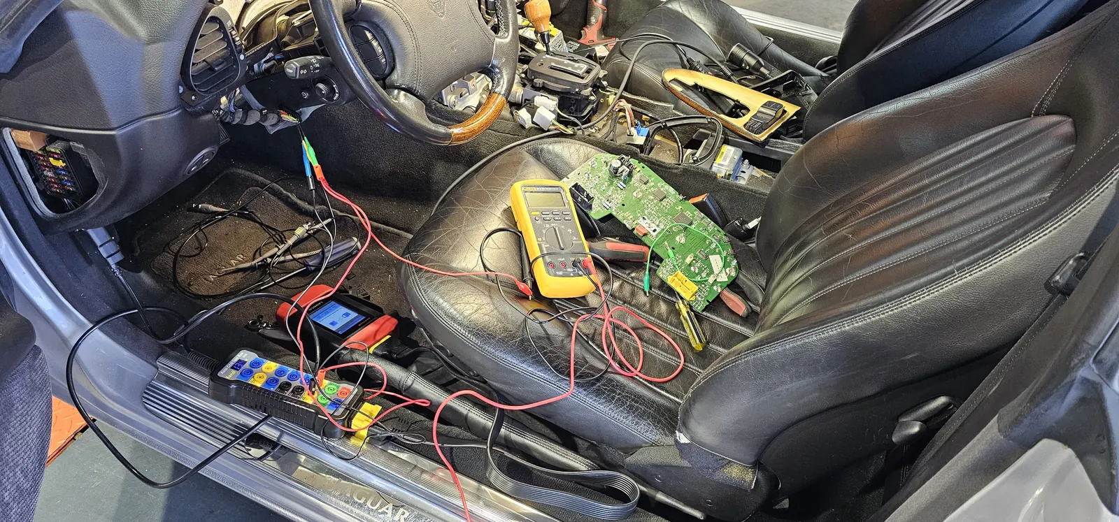 Real-world diagnostics: CAN breakout box, multimeter, and a module on the bench inside a Jaguar