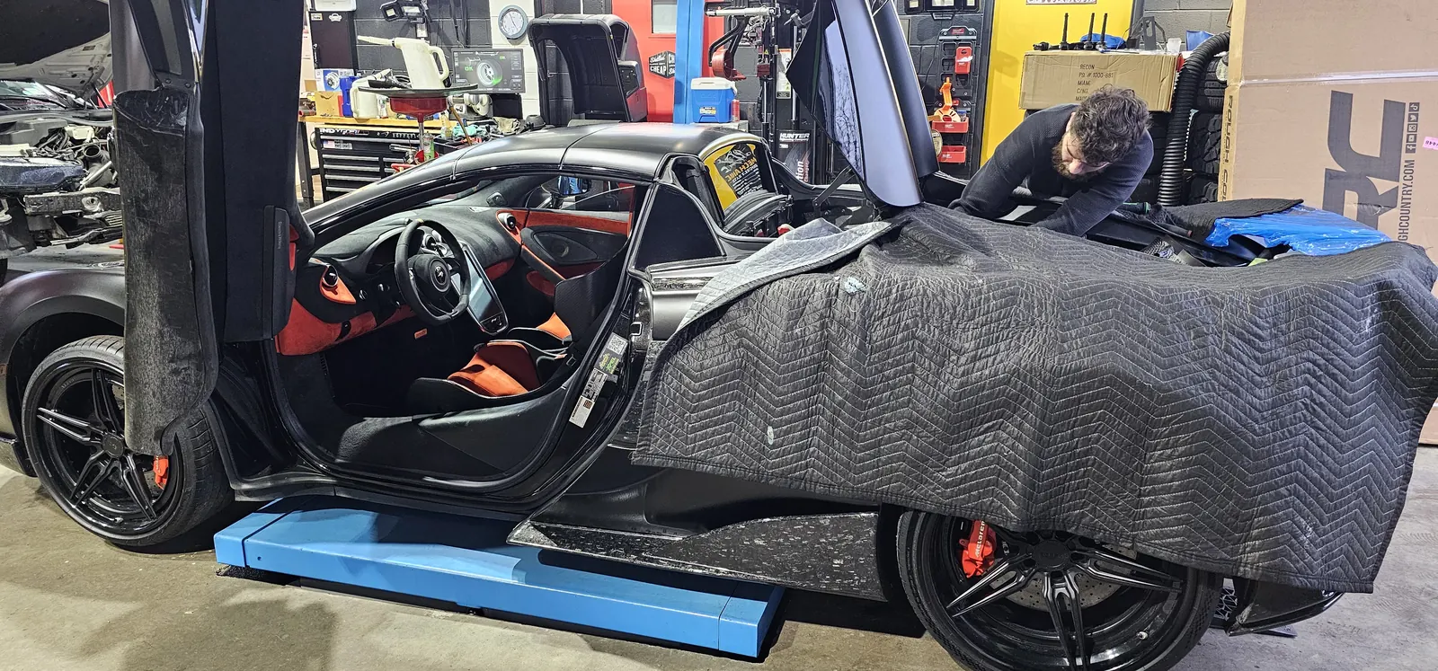 McLaren protected in padded covers while a technician works — the White Glove standard at Prestige Performance Center